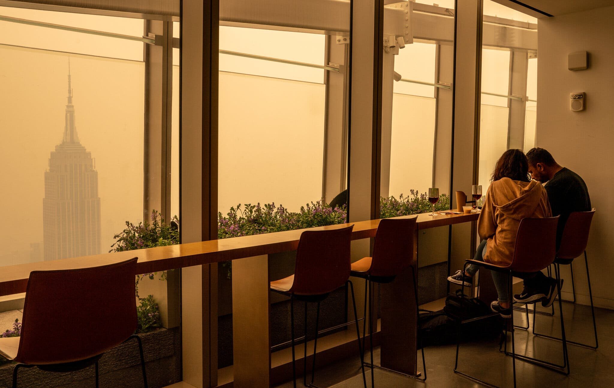 two people sitting in a room while looking out into the wildfire smog in NYC